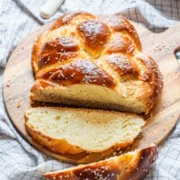 Golden braided Easter bread with sprinkles, sliced and served on a wooden board.