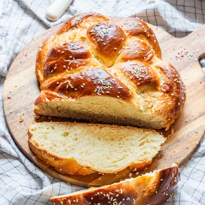 Golden braided Easter bread with sprinkles, sliced and served on a wooden board.