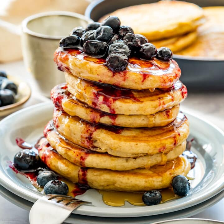 Stack of fluffy pancakes drizzled with syrup and topped with blueberries.