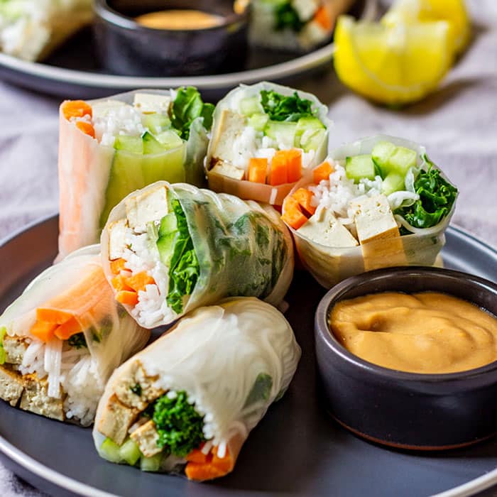 Fresh spring rolls with dipping sauce and lemon wedges.