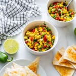Top-down view of a bowl of summer corn salsa with tortilla chips, jalapeño and lime.