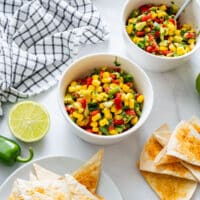 Top-down view of a bowl of summer corn salsa with tortilla chips, jalapeño and lime.