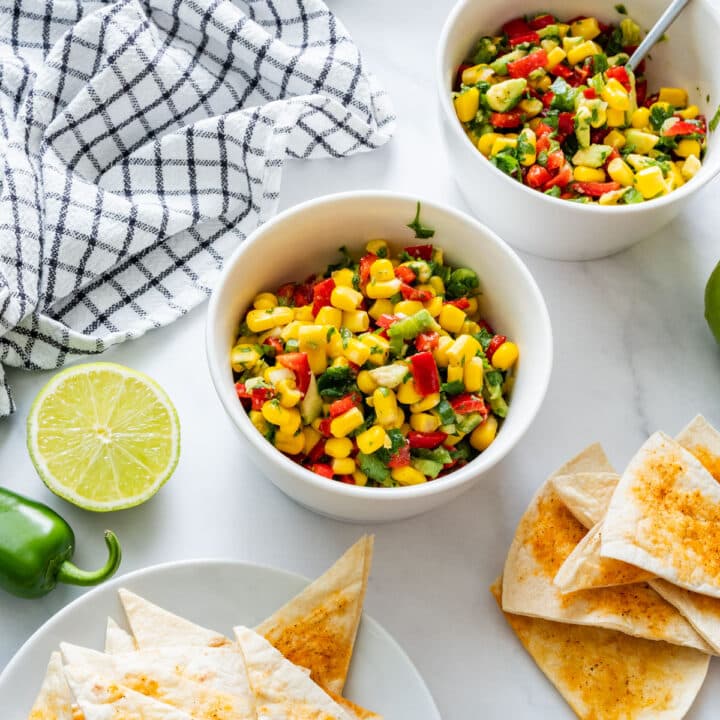 Top-down view of a bowl of summer corn salsa with tortilla chips, jalapeño and lime.