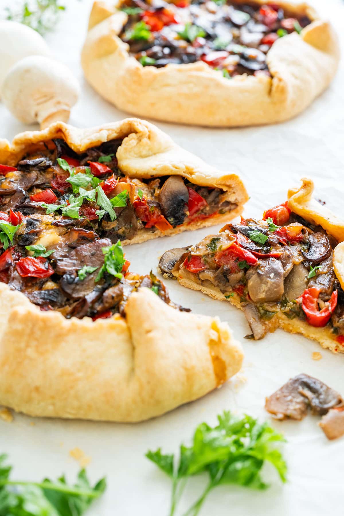 A golden-baked galette with mushrooms, peppers and fresh herbs, sliced open on parchment paper.