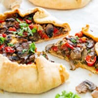A sliced mushroom galette with mushrooms, peppers and herbs, served on parchment paper with fresh parsley.