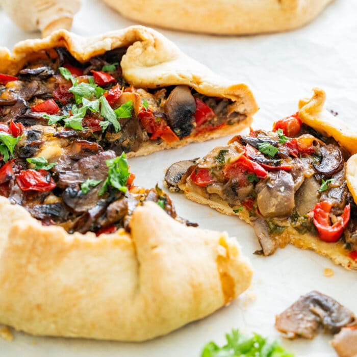 A sliced mushroom galette with mushrooms, peppers and herbs, served on parchment paper with fresh parsley.