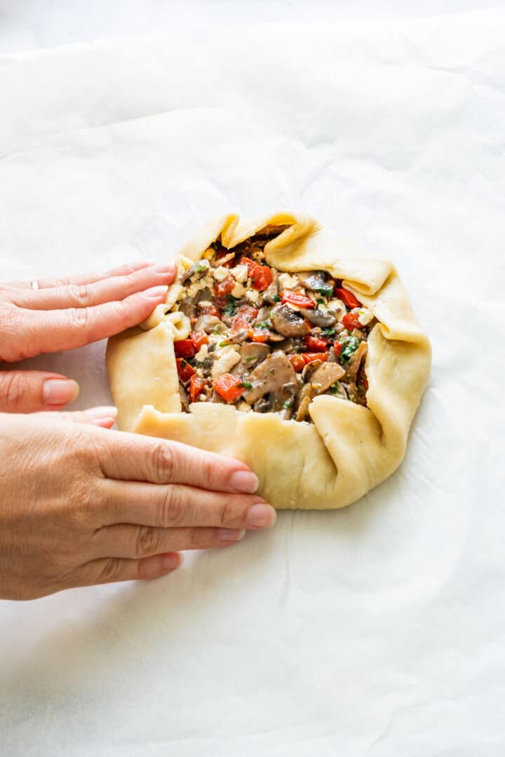 Folding the pastry edges over the vegetable and cheese filling to form a galette.