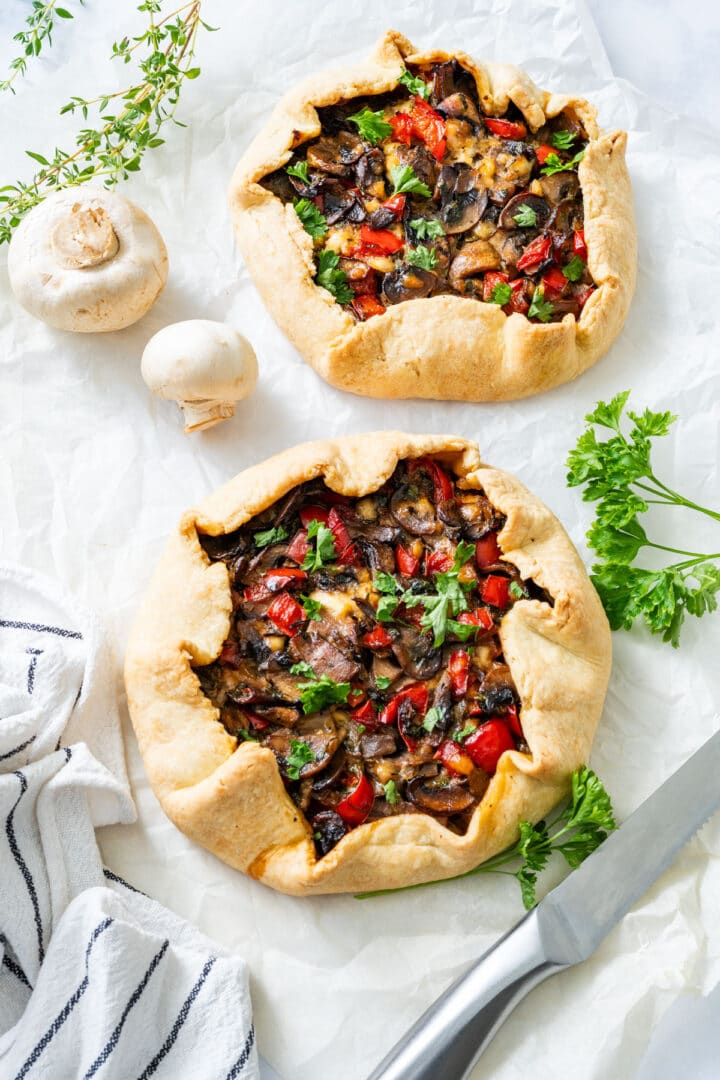 Two baked vegetable galettes on parchment paper, garnished with parsley and thyme.