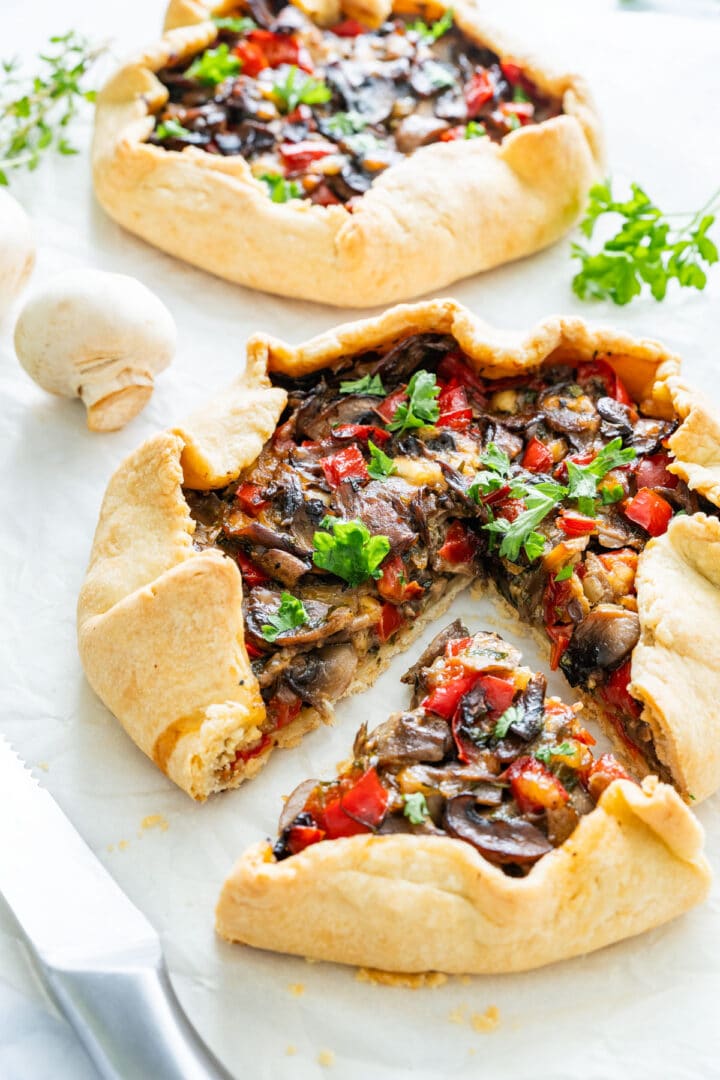 Close-up of a galette with a slice removed, showing the colorful mushroom and pepper filling.