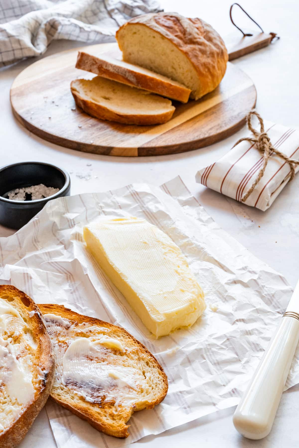 Sliced bread with homemade butter on parchment paper and a buttered toast.