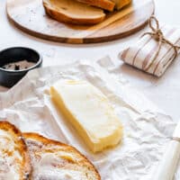 Homemade butter on parchment paper with toasted bread and sliced loaf in the background.