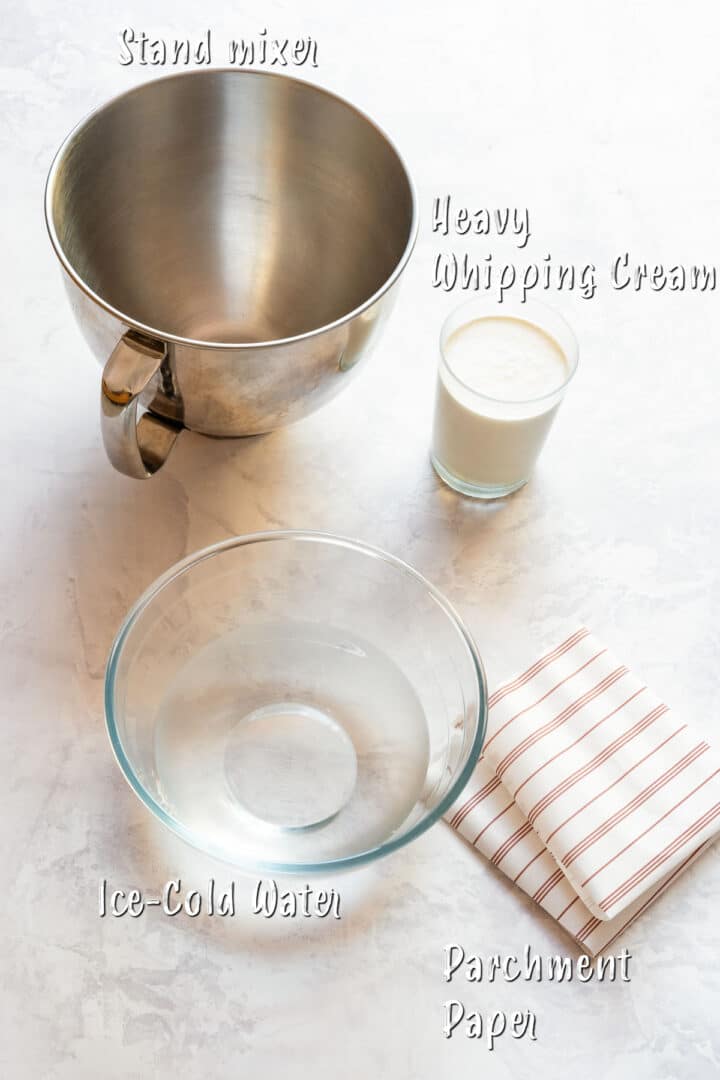 Ingredients for homemade butter including heavy cream, stand mixer, cold water and parchment paper.