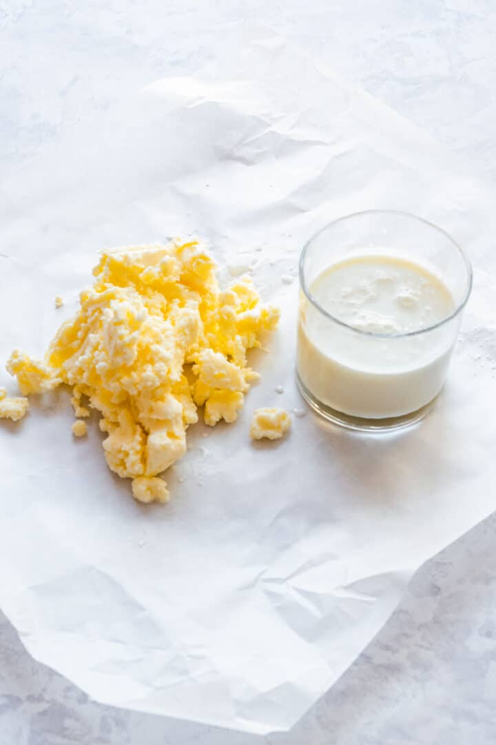 Freshly churned butter and a glass of buttermilk on parchment paper.