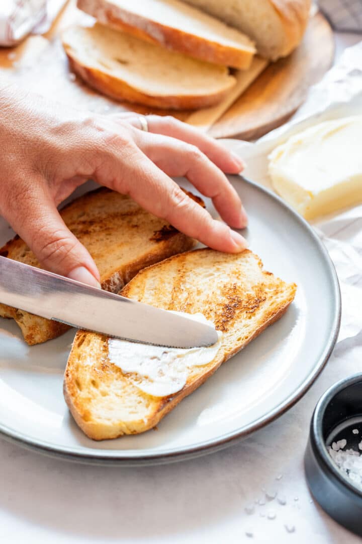Spreading homemade butter on toasted bread slices.
