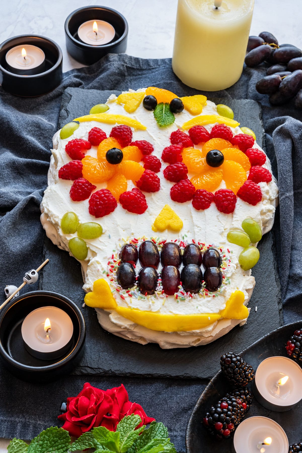 Day of the Dead pavlova with whipped cream and fruit, candles beside.