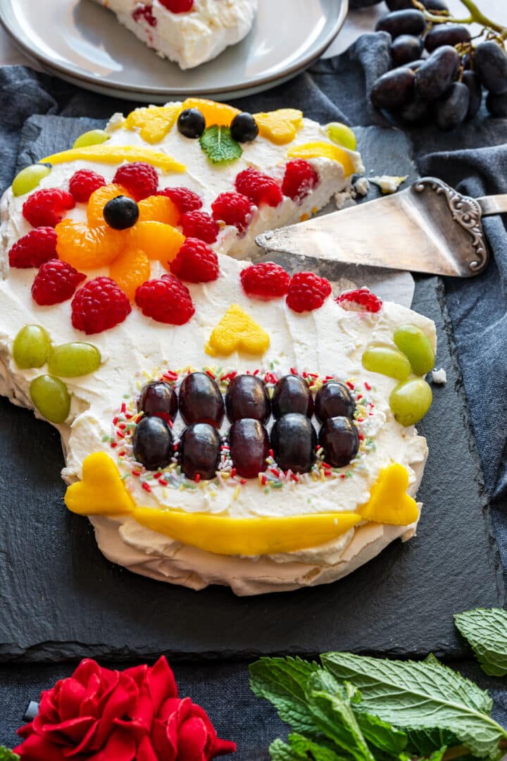 Serving a slice from the pavlova skull, whipped cream and fruit details visible.