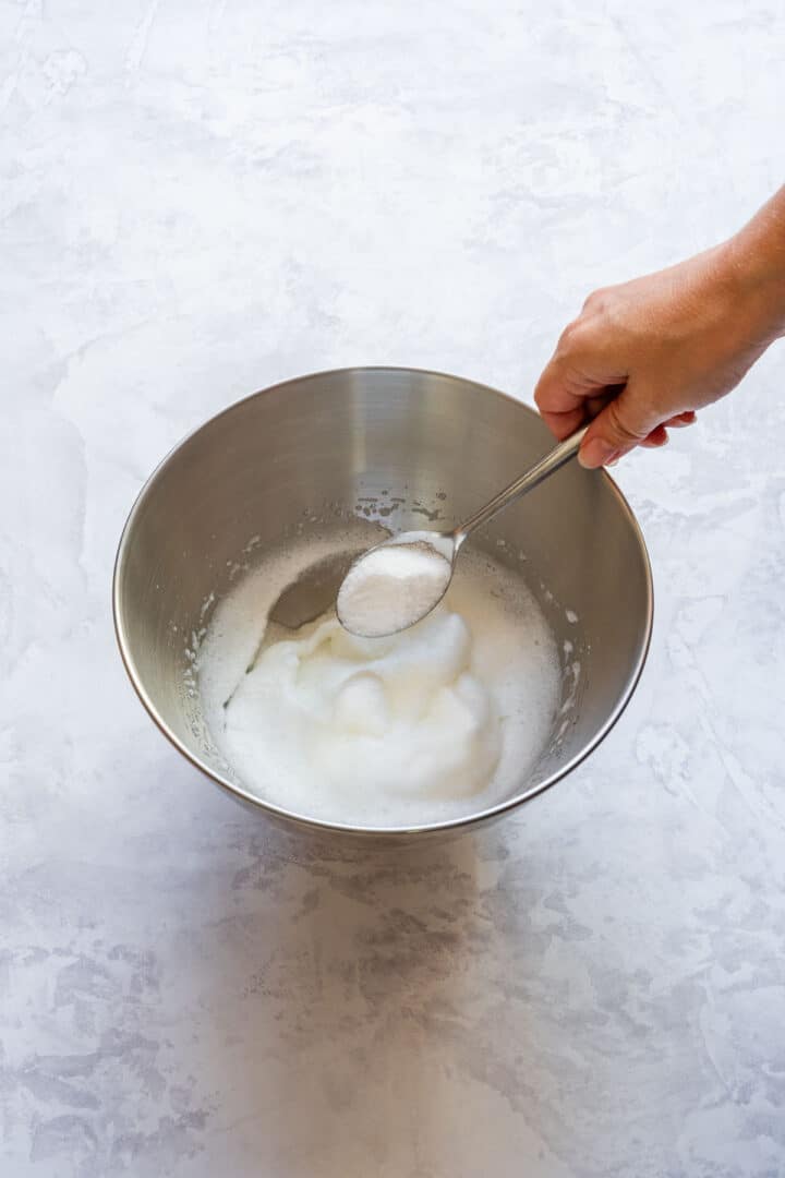 Beaten egg whites in a mixing bowl while gradually adding sugar.