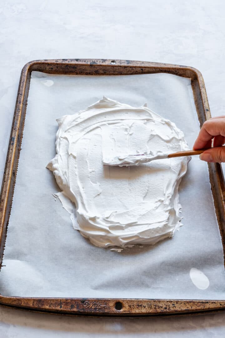 Spreading meringue into a skull shape on a parchment-lined tray.