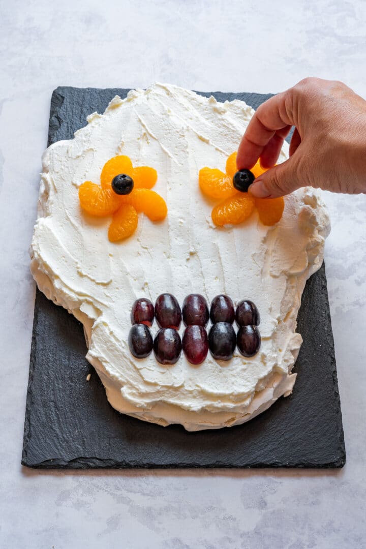 Arranging mandarin segments and blueberries to form the eye decorations.
