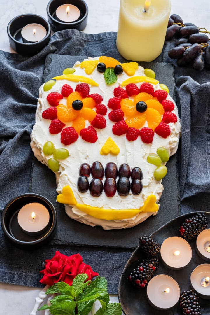 Finished sugar skull pavlova with fruit, candles, roses and mint.