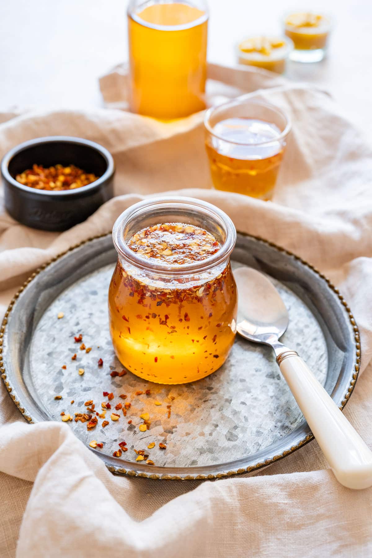 Jar of homemade hot honey with chili flakes on a tray with a spoon.