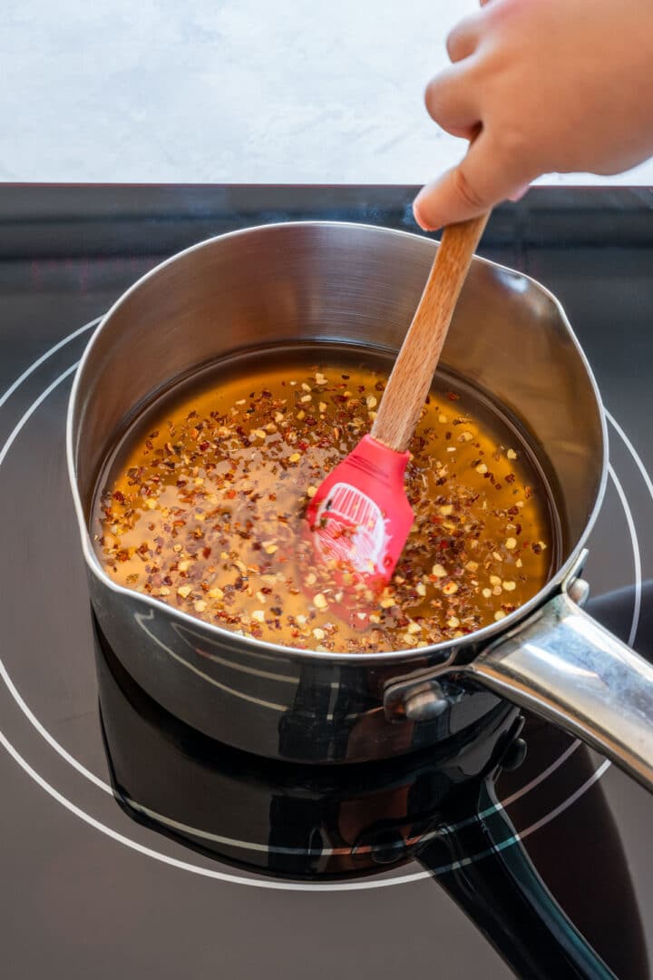 Stirring chili flakes into warm honey in a saucepan.