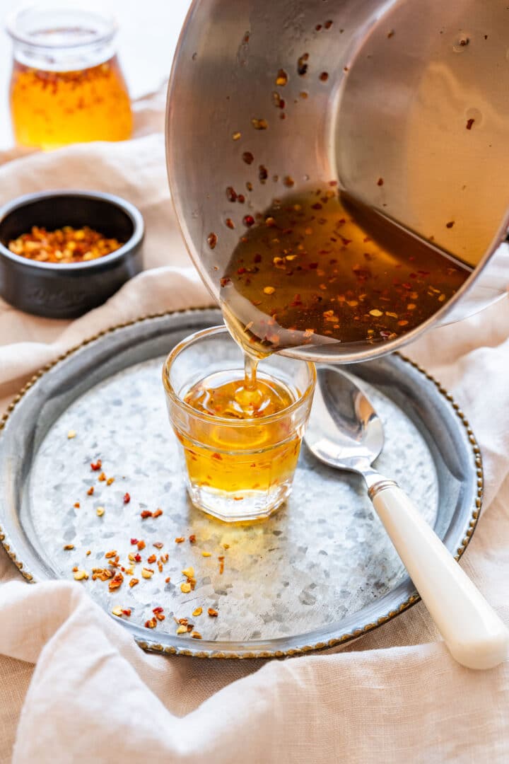 Pouring hot honey from a saucepan into a small glass.