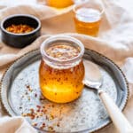 Jar of homemade hot honey with chili flakes on a tray and a spoon beside it.