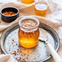 Jar of homemade hot honey with chili flakes on a tray and a spoon beside it.