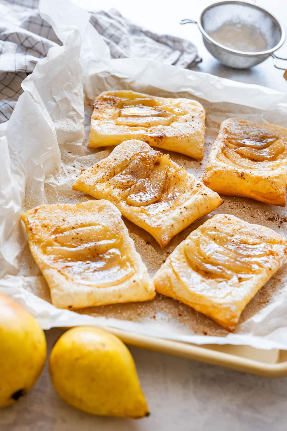 Baked pear tarts on parchment paper dusted with powdered sugar.