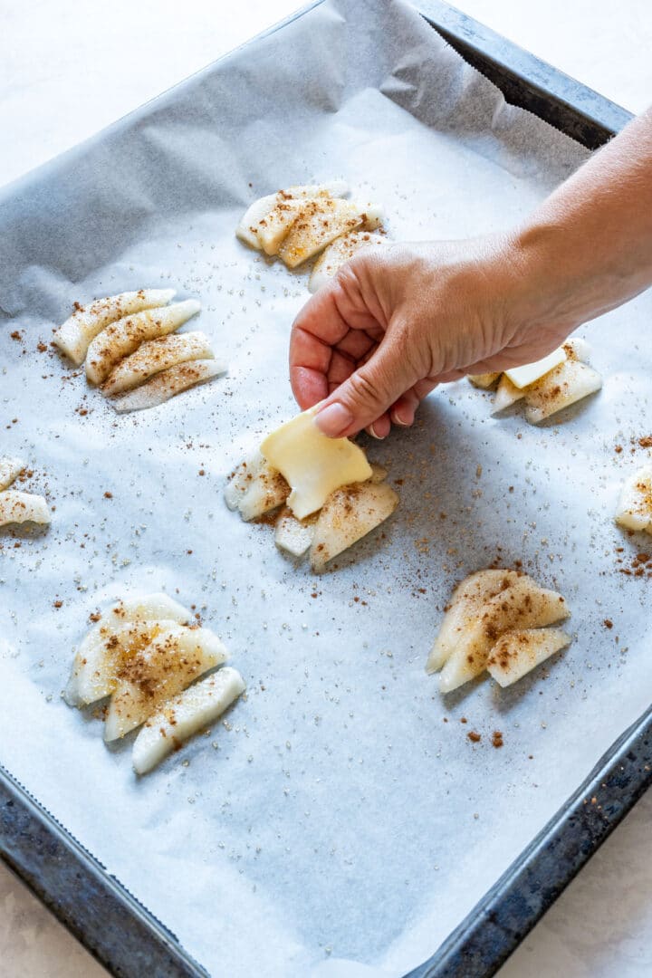 Placing a slice of butter on top of pears sprinkled with cinnamon and sugar.