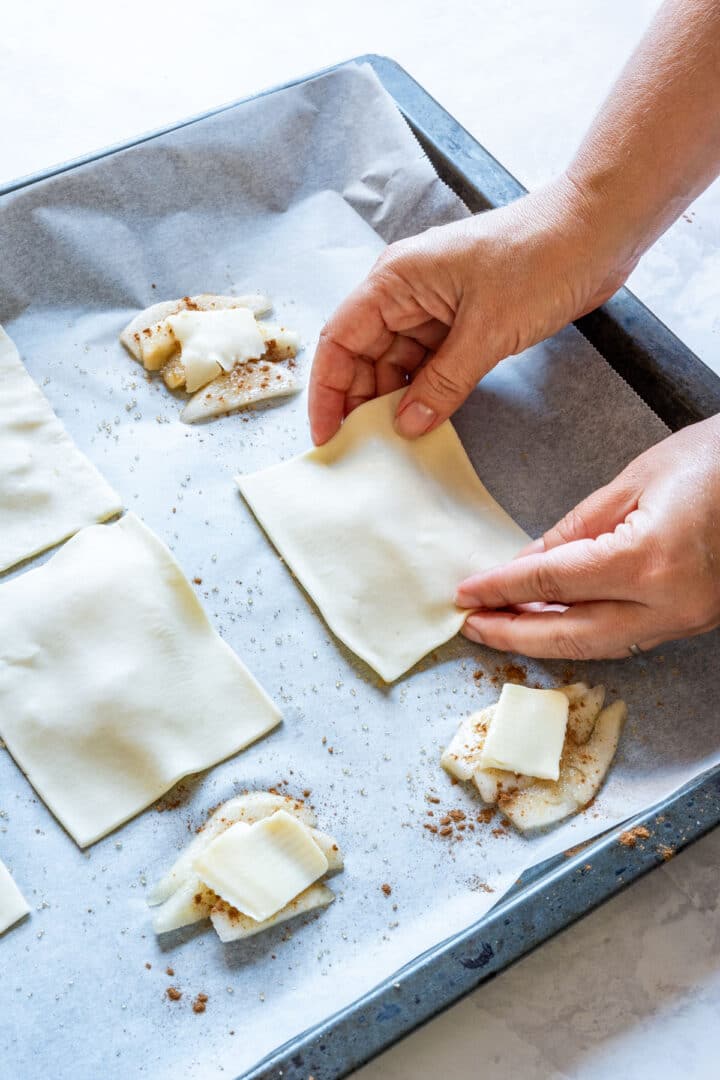 Covering sliced pears with pieces of puff pastry on a baking sheet.