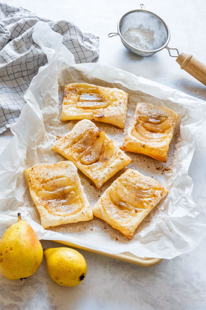 Freshly baked pear tarts cooling on a tray lined with parchment paper.