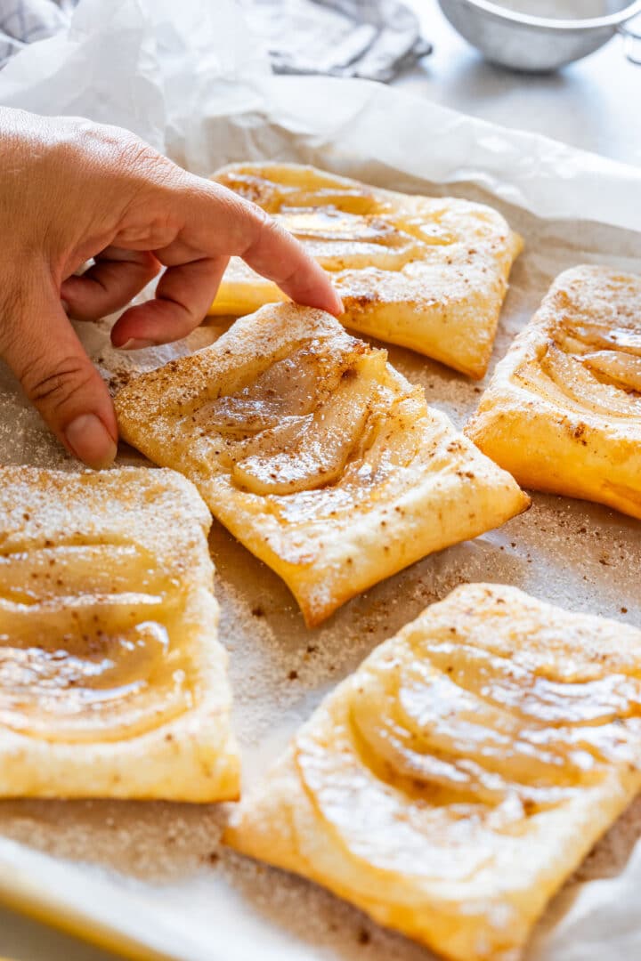 Hand lifting a baked pear tart from the tray.