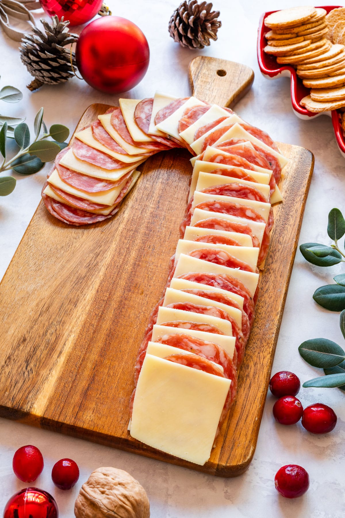 Candy cane ham and cheese board on wooden tray with Christmas decorations.