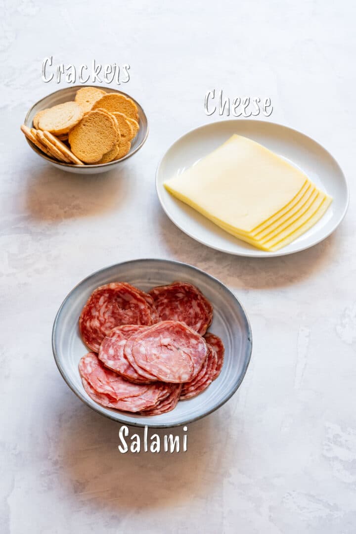 Bowls with sliced salami, stacked cheese slices and crackers for candy cane board.