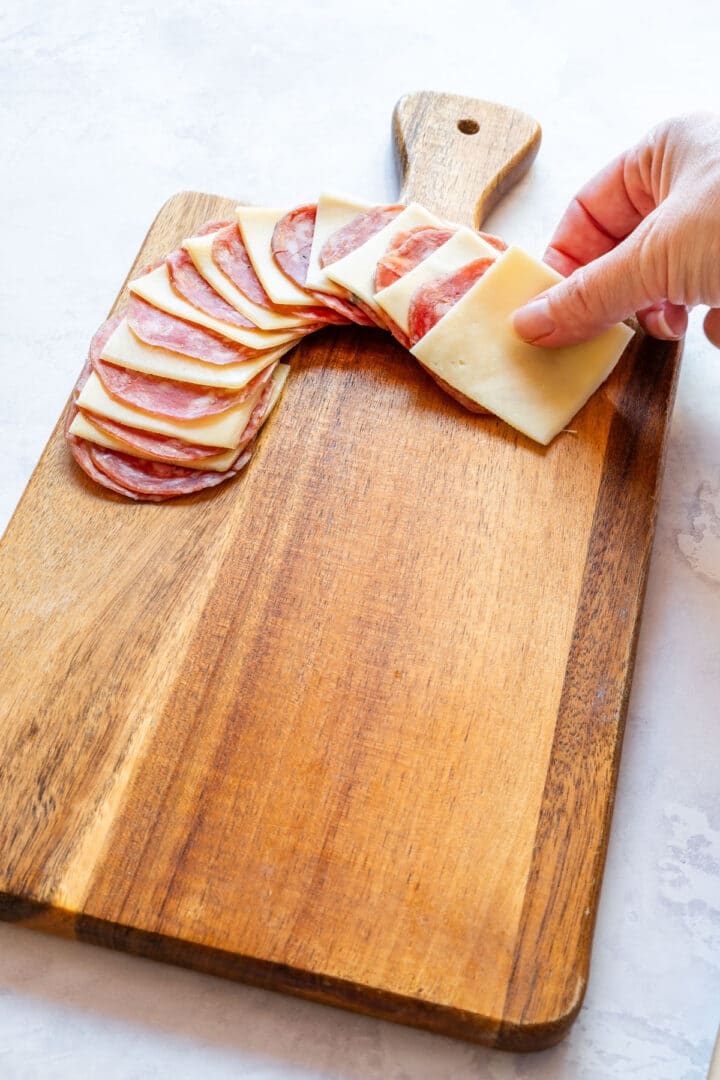 Arranging salami and cheese slices into a curved candy cane shape on board.