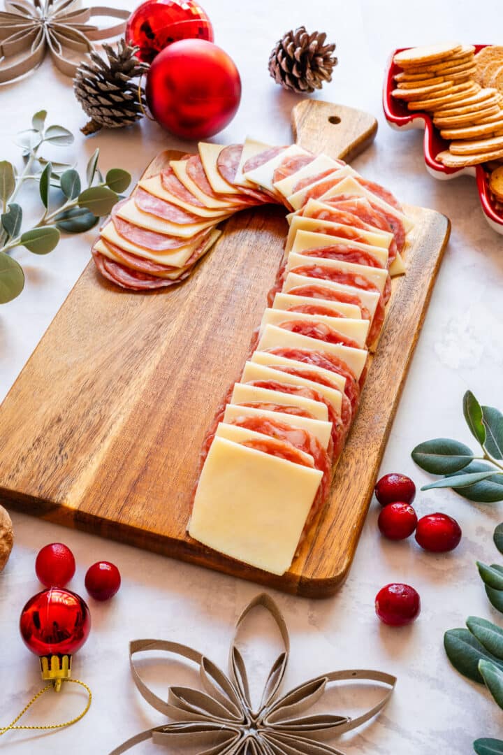 Christmas snack board with candy cane shaped salami and cheese rows on wooden board.