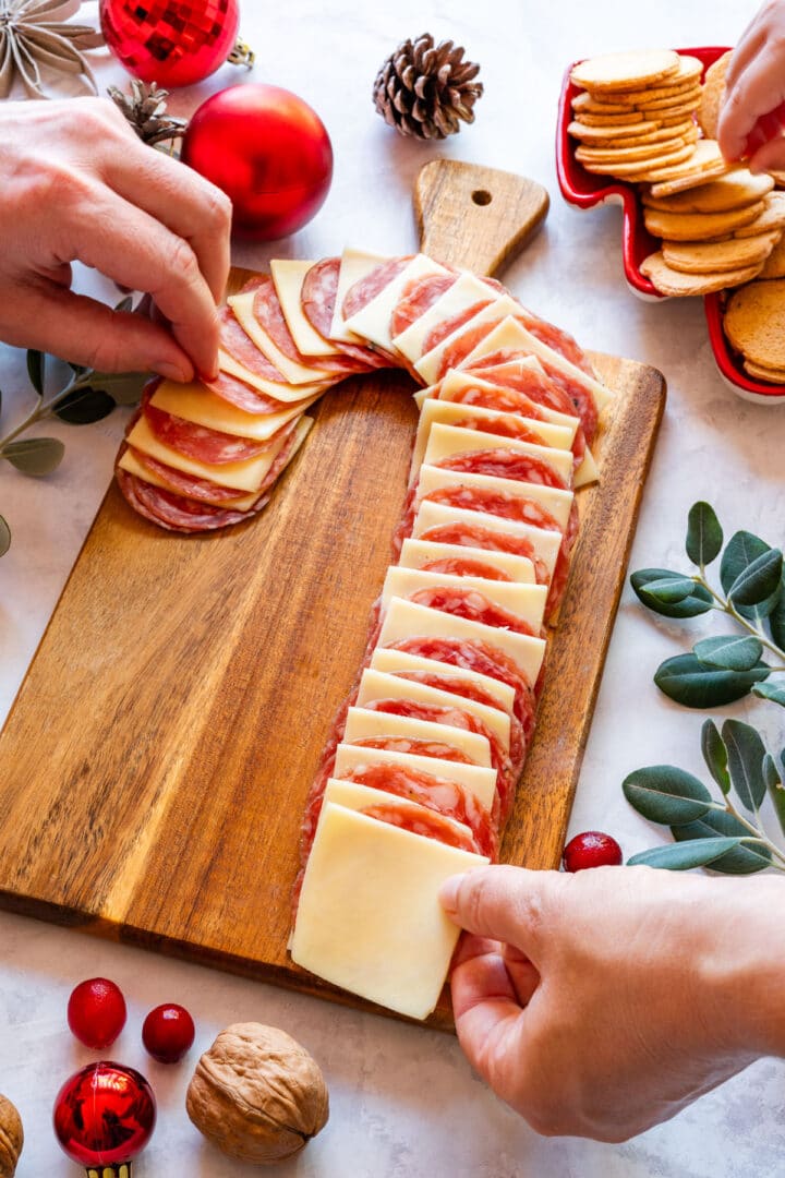 Hands reaching for salami, cheese and crackers from the finished candy cane appetizer board.