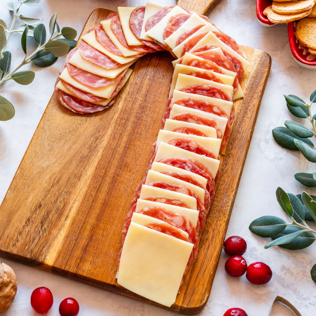 Candy cane ham and cheese board on wooden serving board with cranberries and greenery.