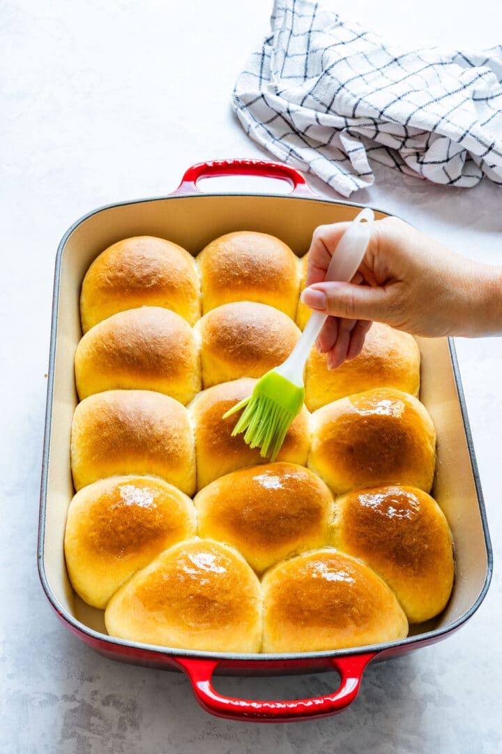 Brushing melted butter over the tops of freshly baked sweet potato dinner rolls.