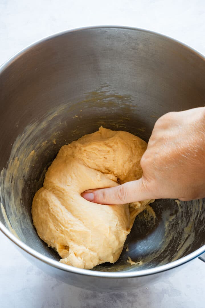 Pressing a finger into the dough to check if it is smooth and not sticky.