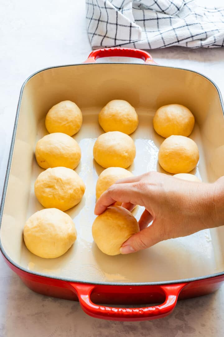 Placing dough balls into a greased red baking dish in neat rows.