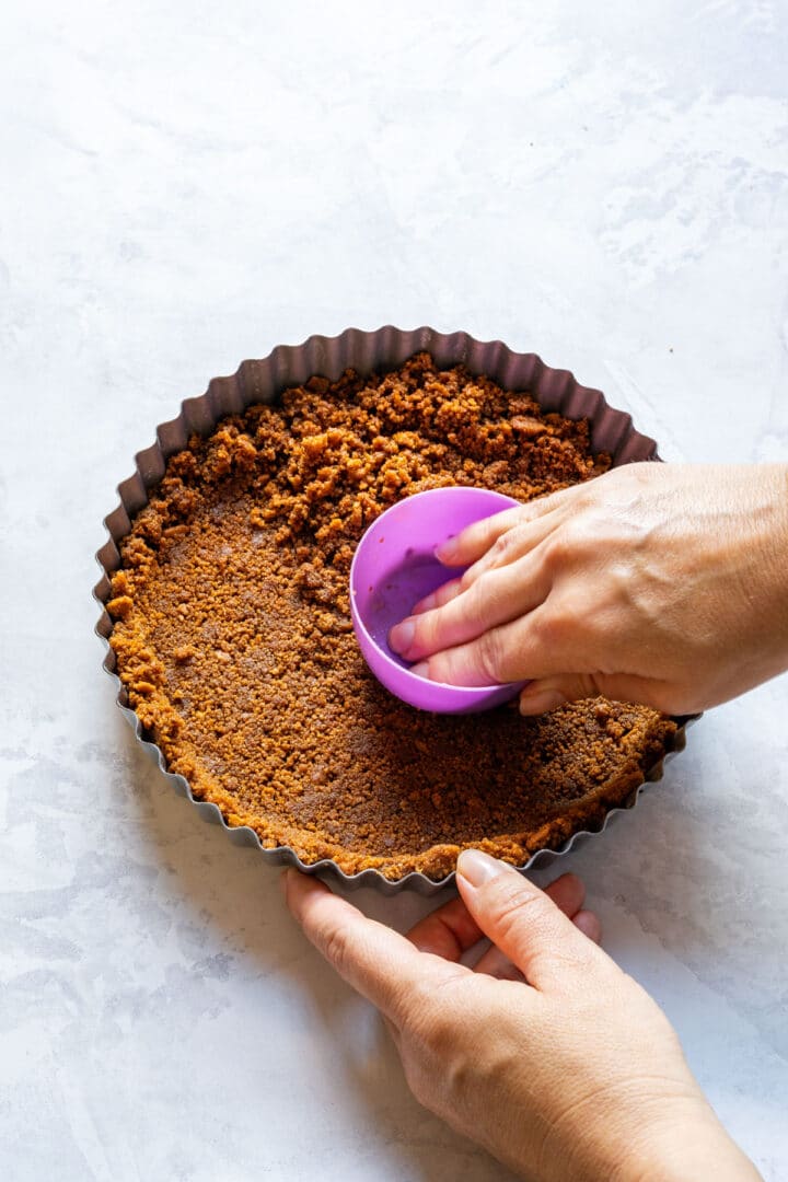 Pressing cookie crumbs into a fluted tart pan.