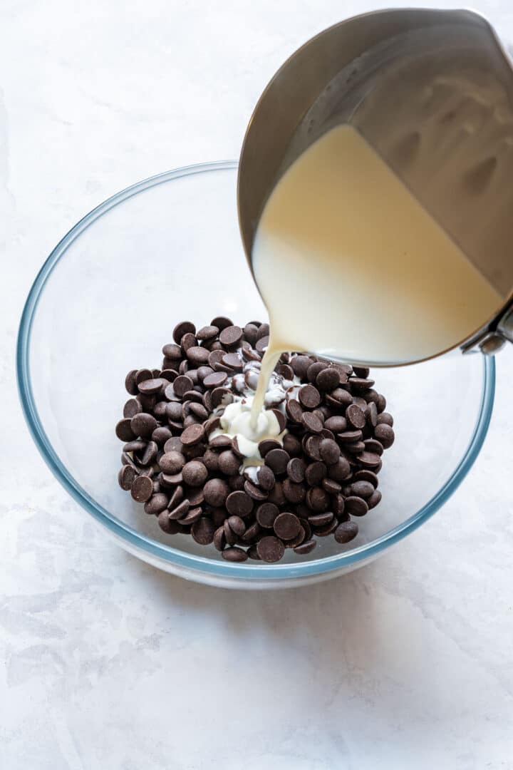 Pouring hot cream over dark chocolate buttons to start the ganache.