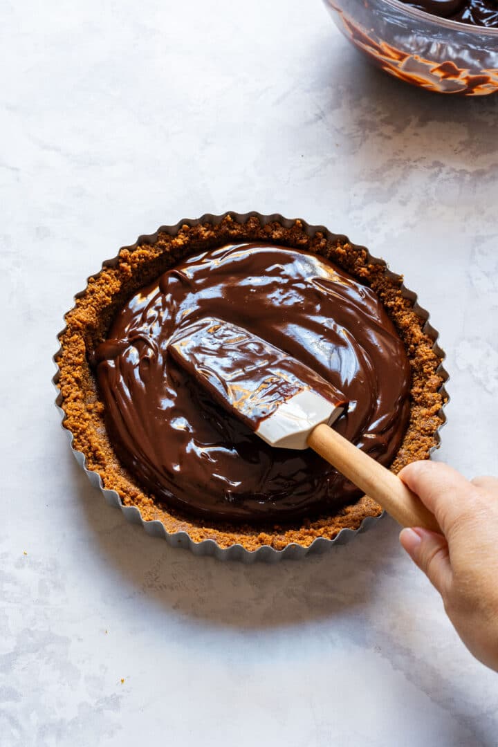 Spreading dark chocolate ganache into the chilled cookie crust.