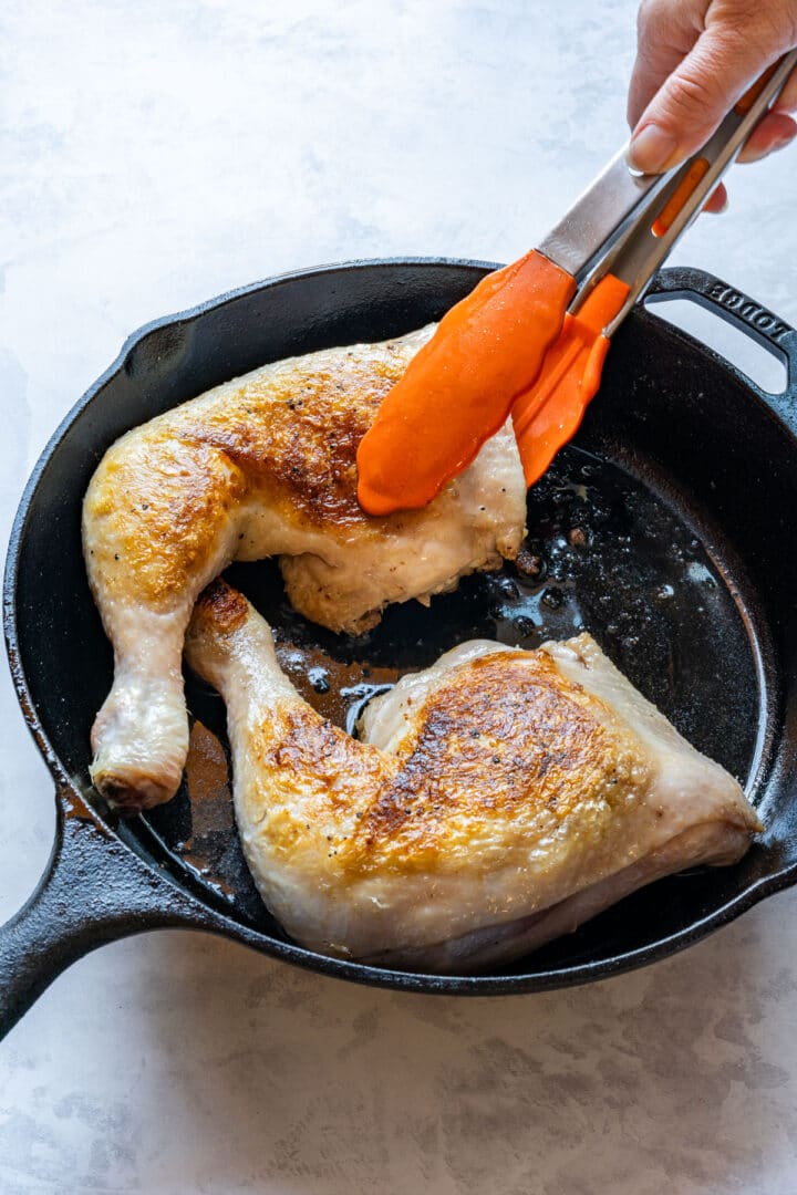 Searing a chicken leg quarter skin side down in a cast iron skillet.