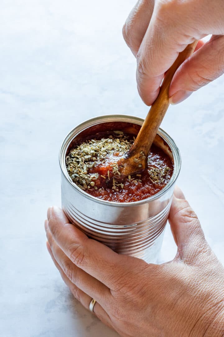 Stirring dried oregano into tomato sauce in an opened can.