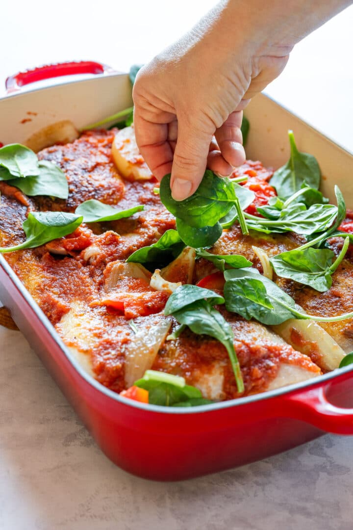 Adding fresh spinach to the baked chicken and tomato sauce before serving.