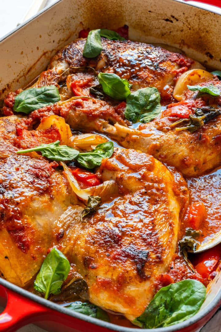 Close-up of tender chicken in tomato sauce with bell pepper, onion and spinach.
